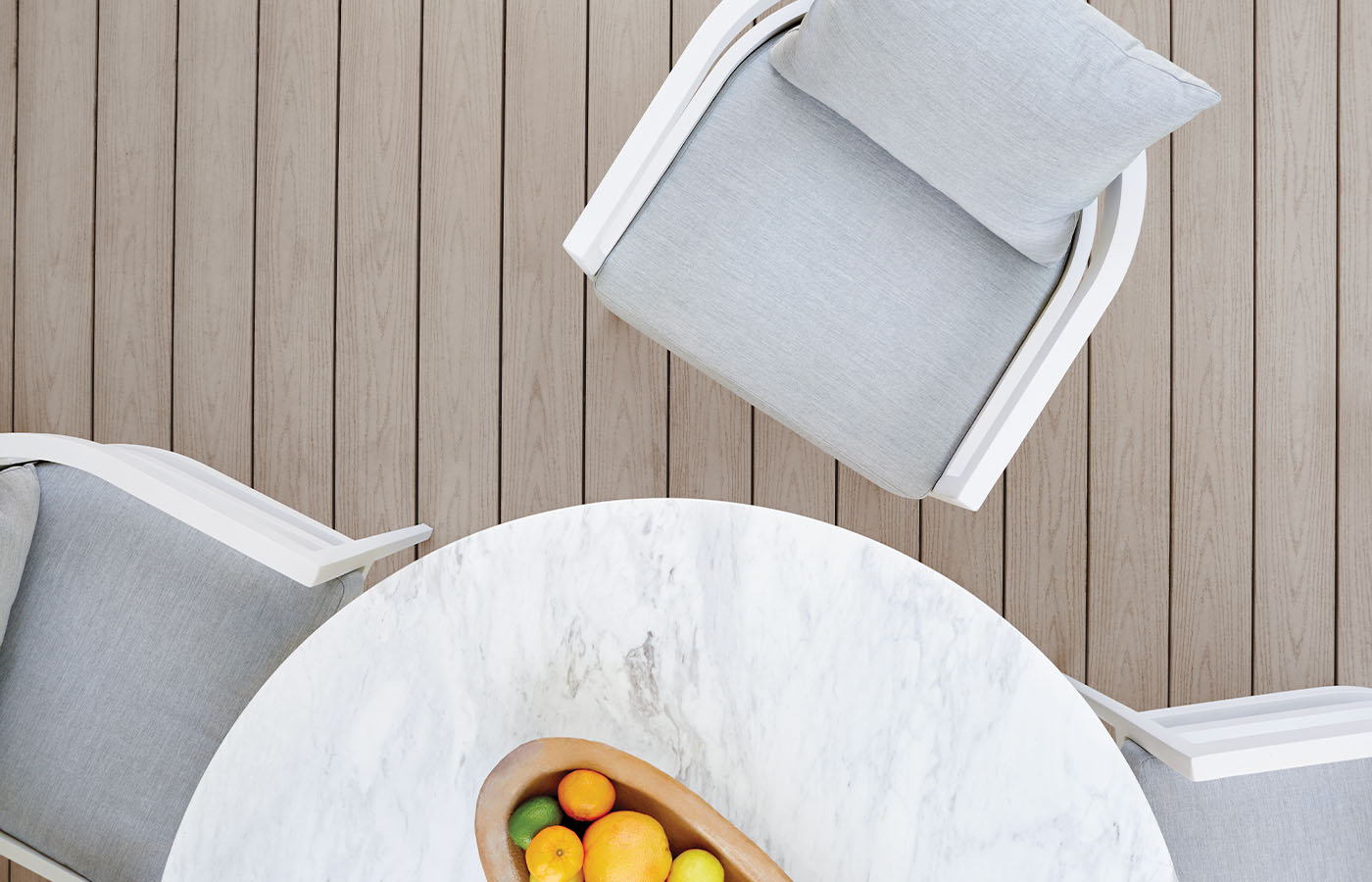 A white and gray chair next to a lighter gray table with citrus fruits in a brown basket seen from above.