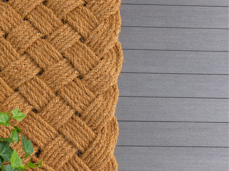 Close up photo of a woven mat atop the gray porch boards
