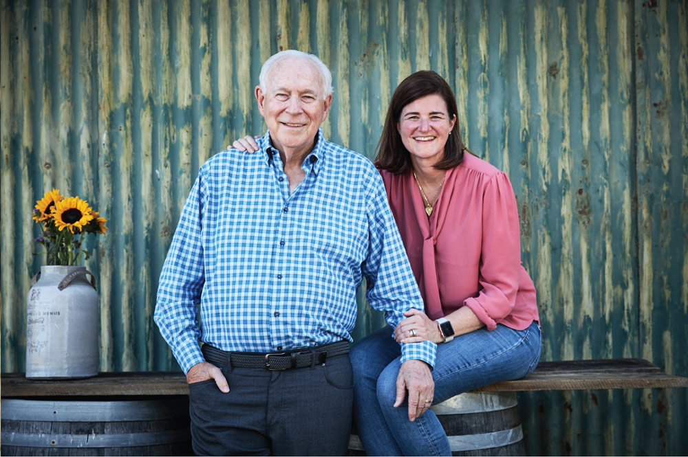 Headshot of Tricia and family against a steel wall with a brown table of held up by brown barrels in the mid-ground. 