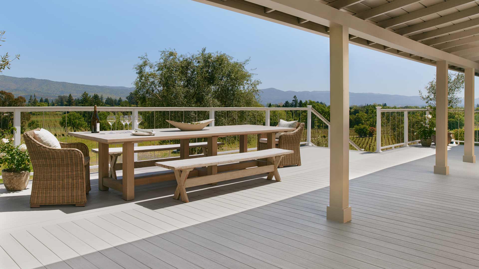 A patio view of Napa Valley with brown decking, a wooden table and wicker chairs.