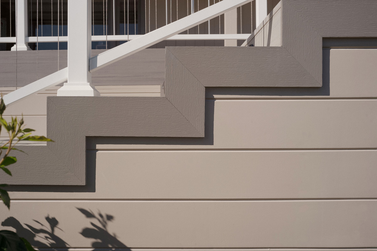 A detailed view of the white stair rail connecting to the home. The stairs are decorated with gray trim boards and brown decking. 