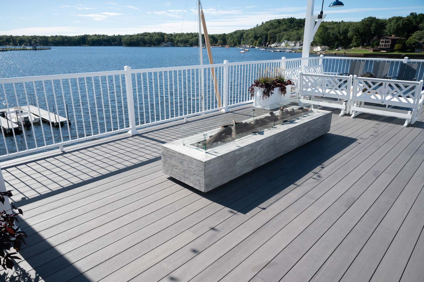 A gray deck that looks out onto the water and is accented with concrete planters and white planters accented with purple and green plants. 