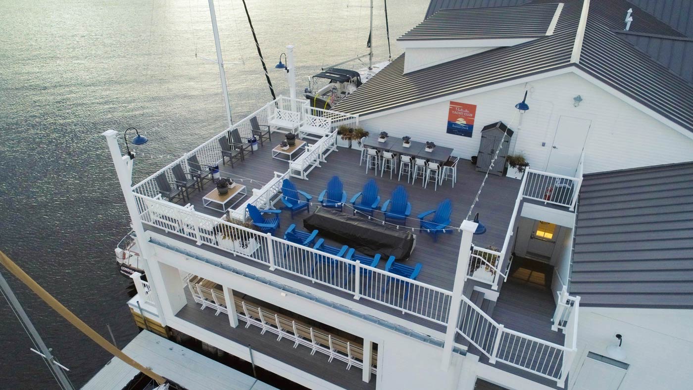 An view from above a deck with gray decking and blue chairs. White railing surrounds the deck and gives a view of the water.