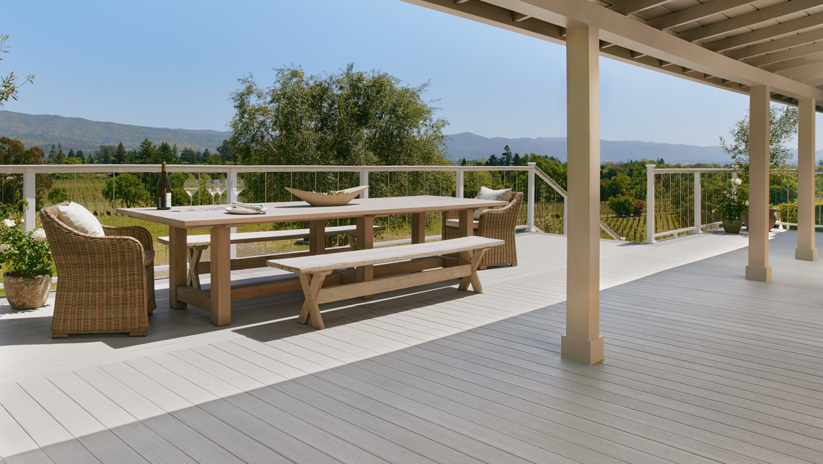 Patio with light grey decking looking out over a green winery and mountains in the distance. 