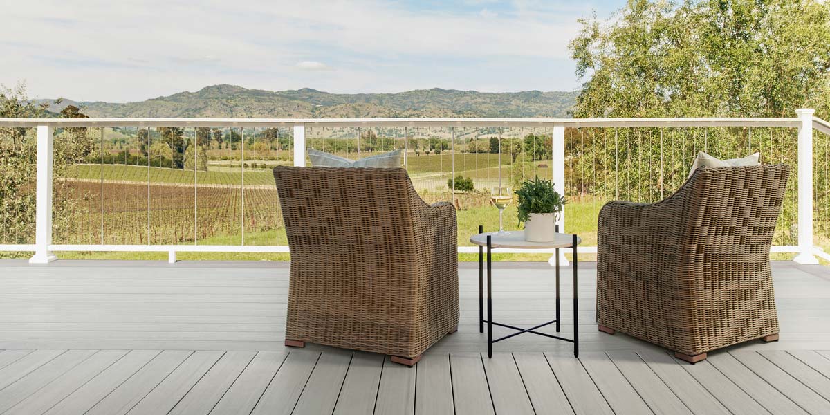 Two wicker chairs on deck with white Impression Rail Express rail with a vertical cable rail infill