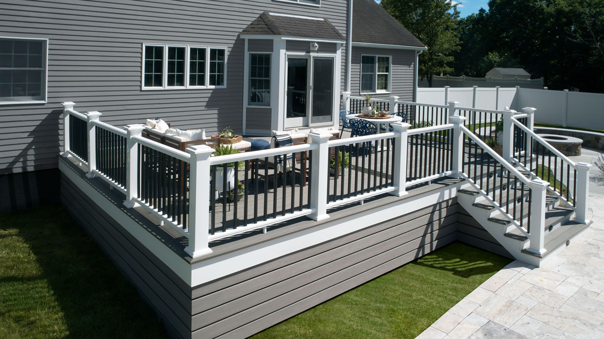 A white railing with black baluster infill contrasts with the gray deck of a house.