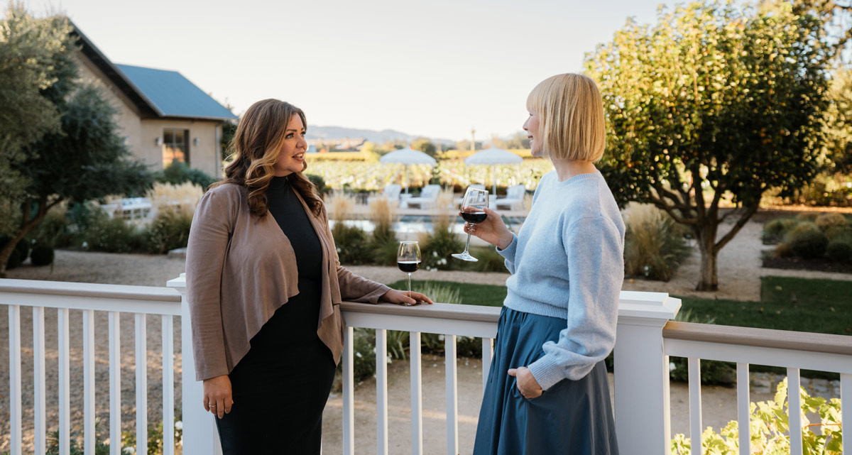 Two women talk over glasses of wine, TimberTech Drink Rail acts as a surface to rest their glasses as they chat