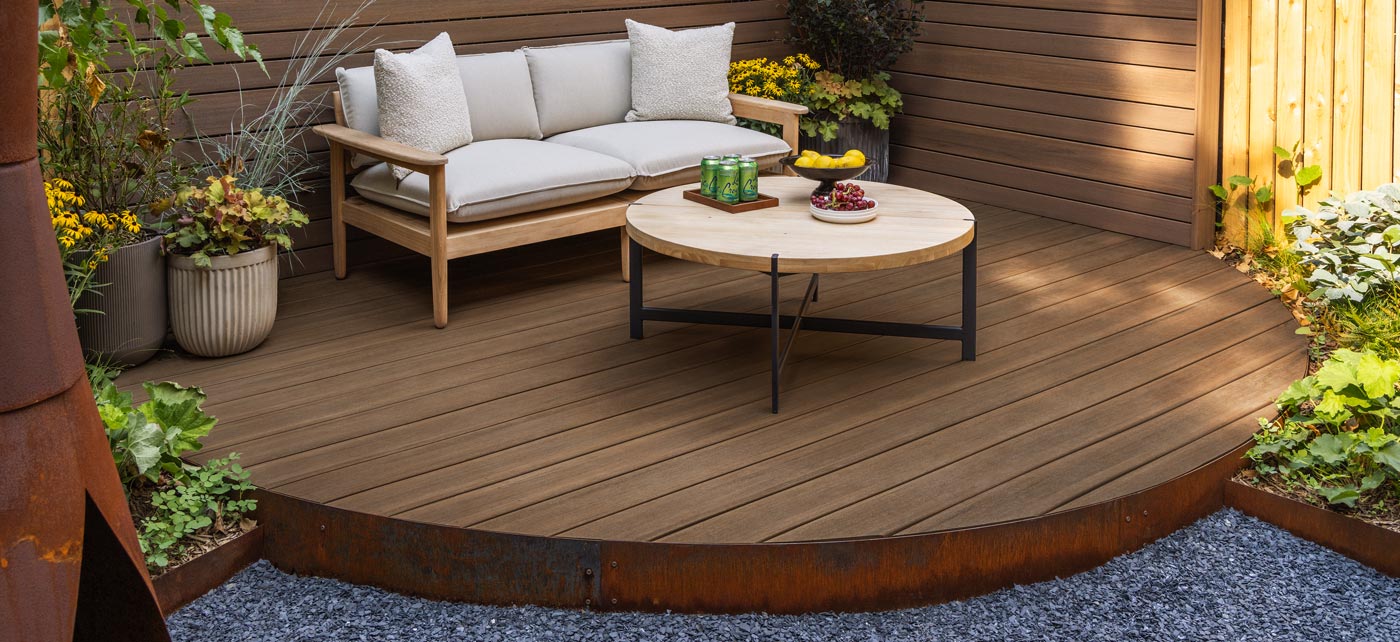 A view of the backyard island deck decorated with a privacy wall and decking from the Advanced PVC decking from the Vintage Collection. The decking uses standard width boards and narrow boards to a create ambiance of privacy for outdoor gatherings. The landscape design was created by Brooklyn Grange and the decking designs were created by Decks R Us.