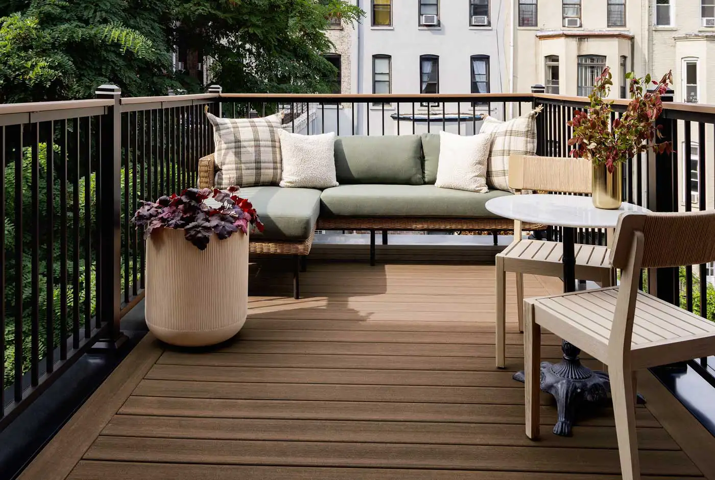 The new Brooklyn brownstone rooftop deck with a couch, two chairs and table. It is trimmed with Aluminum Framing in Classic Black. The light brown decking is English Walnut from the Vintage Collection. The soft glow of the sun illuminates the light pale green couch cushions. 