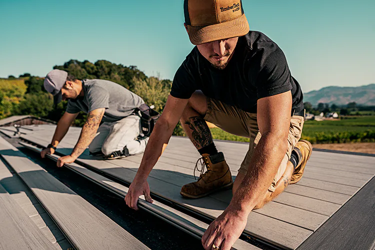 Two TimberTech Contractors place a deck board down during a deck build